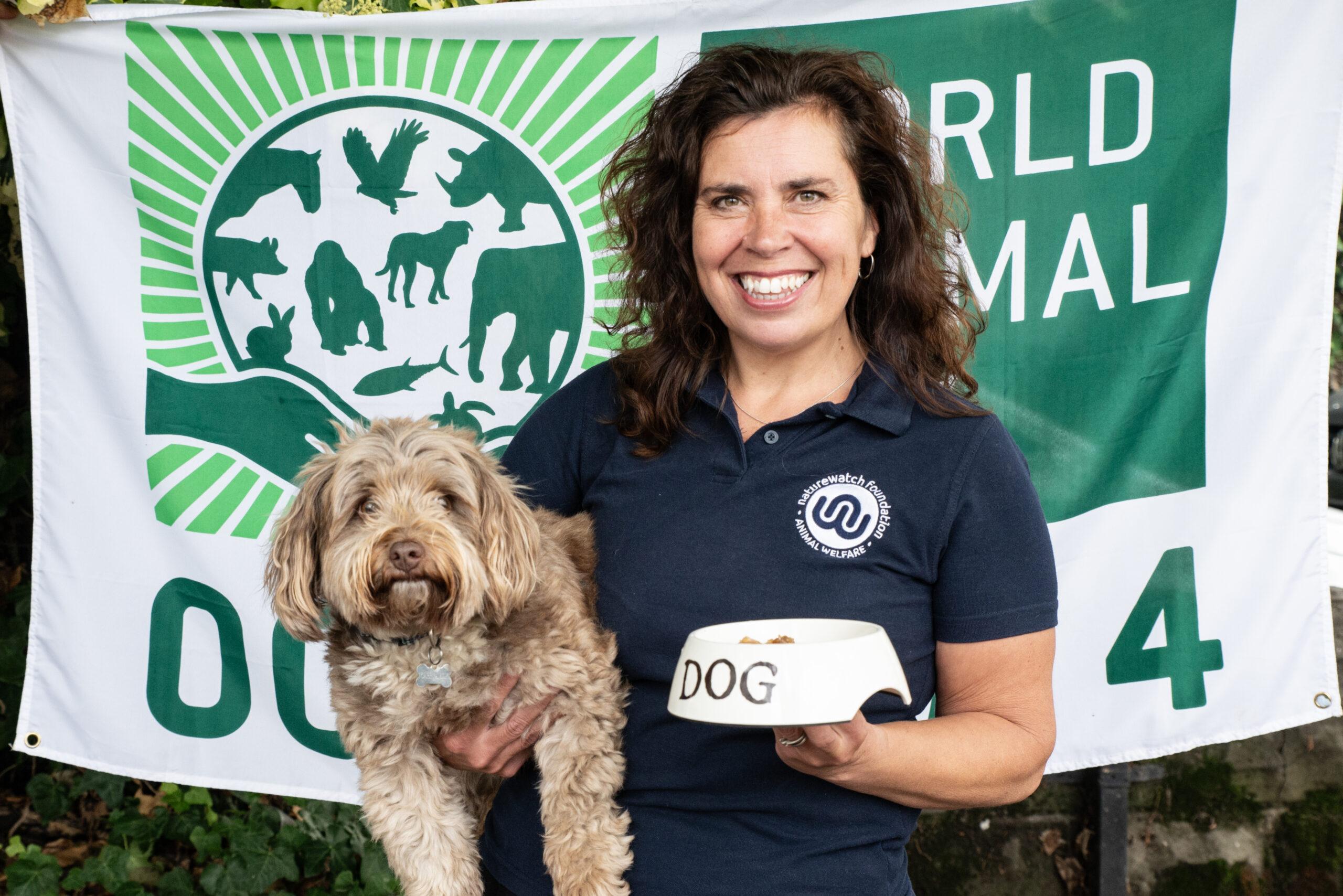 Sarah our CEO, with her dog Buddy, holding a bowl of dog food in front of the World Animal Day flag.