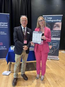 Mark with Detective Superintendent Kris Windsor: Image shows Campaign Manager, Mark Randell, smiling for a photograph next to Detective Superintendent Kris Windsor. Kris is holding up a Protect Animals, Protect People Campaign Factsheet. They are standing in front of a display named 'Loop Safeguarding'
