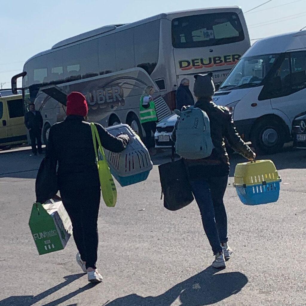 The war in Ukraine: How Naturewatch Foundation has been supporting animals in crisis 2 Two people in winter clothing are walking away from the camera, holding pet carriers, a cardboard carrier and bags. There’s a bus and a van in the background.