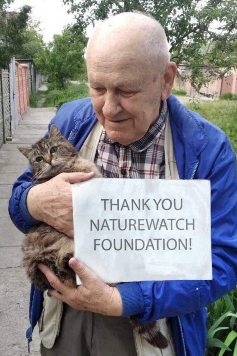 Your support 12 A man holds a tabby cat and a sign reading "Thank You Naturewatch Foundation" outdoors. He wears a plaid shirt and blue jacket, smiling warmly.
