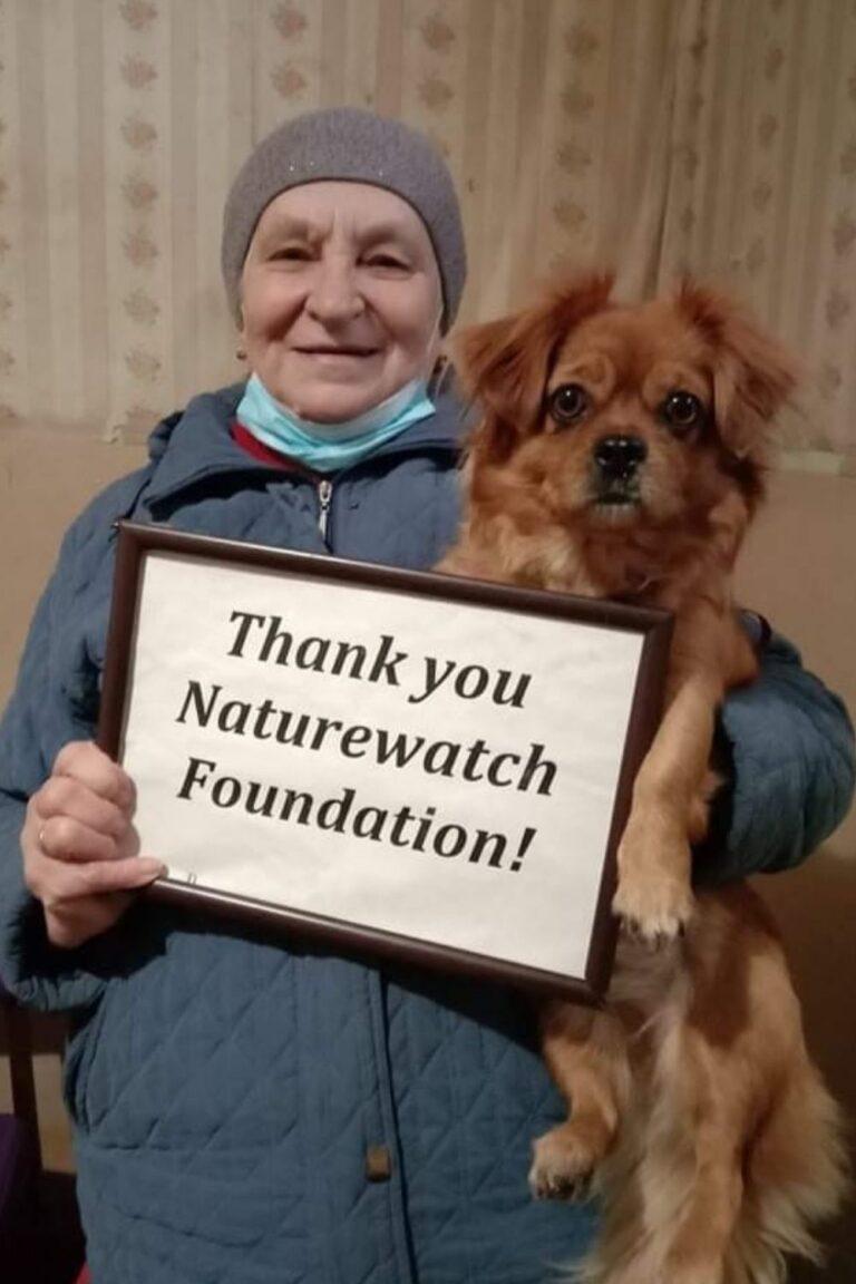 Your support 4 A woman, smiling, holds a small brown dog and a framed sign reading, "Thank you Naturewatch Foundation!"
