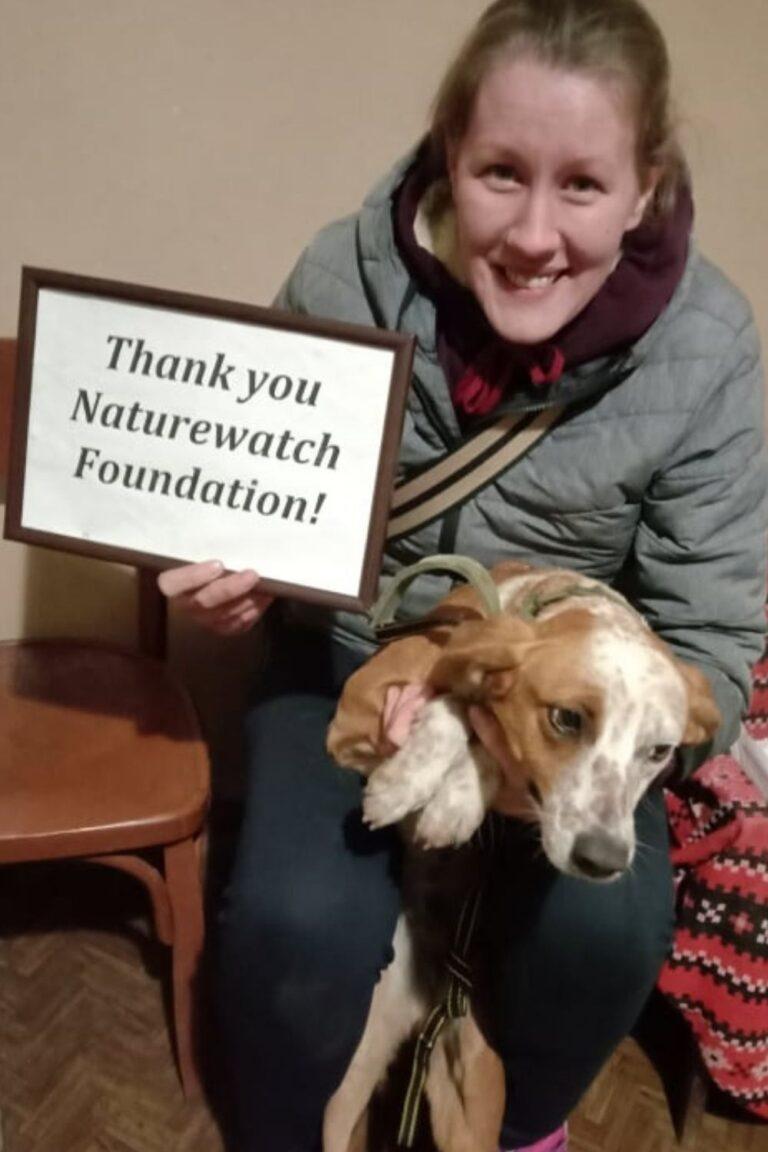 Your support 6 A smiling woman holds a small brown and white dog and a framed sign that reads "Thank you Naturewatch Foundation!"