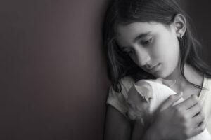 A black and white photo of a young girl holding a small puppy against her chest.