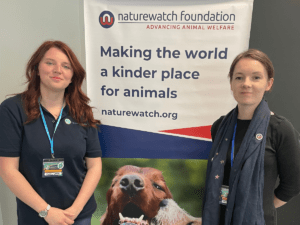 Two women standing in front of a Naturewatch banner that says 'Making the world a kinder place for animals'.