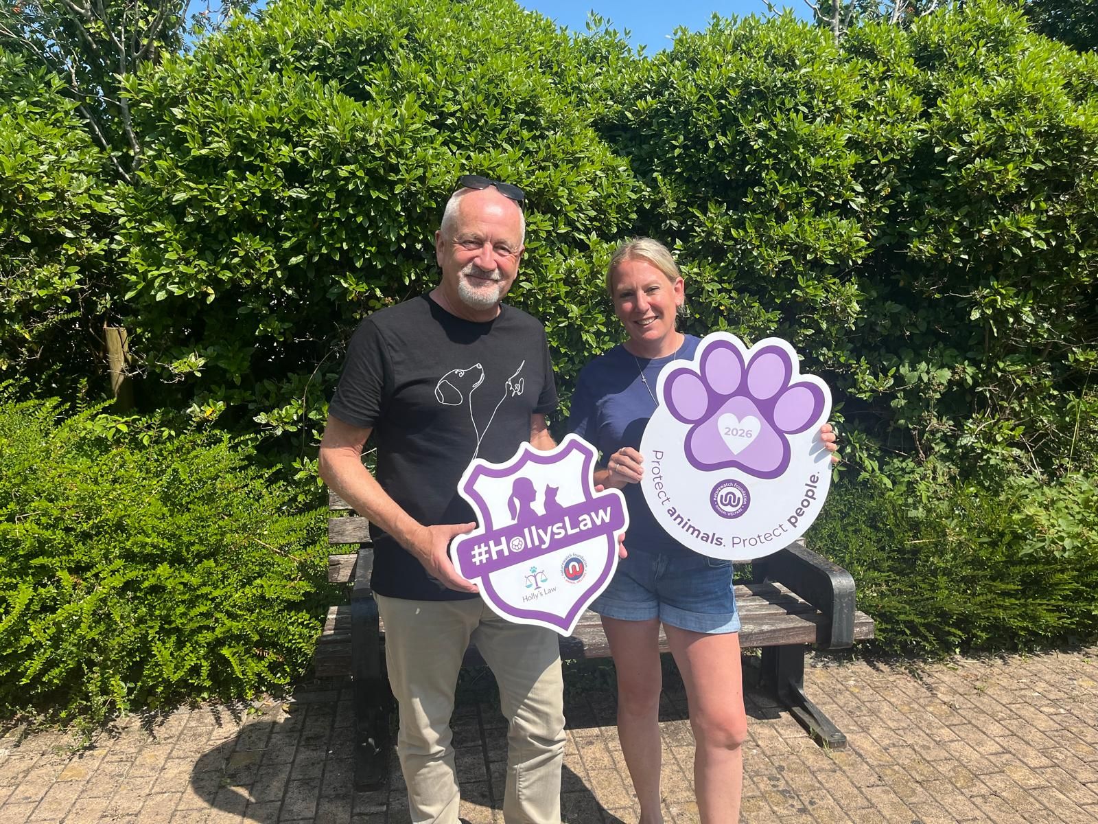A Shared Mission: Why Naturewatch Foundation and Refuge4Pets Are Working Together 2 Two people stand outdoors holding purple and white Holly's Law and Purple Paw campaign signs.