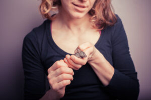 A woman with short brown hair and a navy blue v-necked top gently holds a small mouse in her hands.